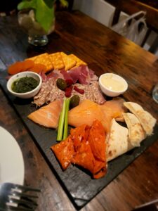 A charcuterie board with crackers, olives, pepperoni, chorizo, salmon, pesto