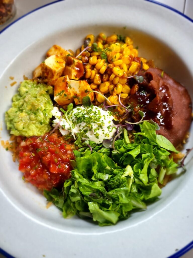 A vegetraian burrito bowl with corn, paneer, guacomole, salsa, lettuce, red beans, sour cream